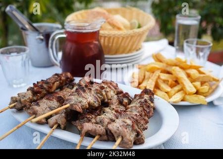 focalizzazione selettiva sulla carne di layout tipico della tavola greca, tra cui la brocca da mezzo litro di vino rosso, patate fritte, souvlaki e pane Foto Stock