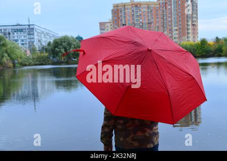 Ragazzo con un ombrello in autunno. Capretto è smilling. Dietro la schiena del ragazzo magnifico albero giallo del lago e della città. Tenere un ombrello dentro Foto Stock