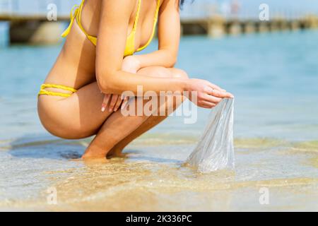 Un volontario femminile raccoglie plastica sulla riva dell'oceano Foto Stock