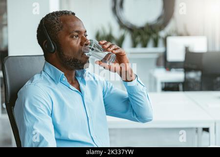 Uomo d'affari africano che indossa cuffie acqua potabile mentre si è seduti in ufficio Foto Stock