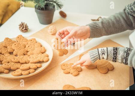 La mano del ragazzo e la mano del padre tengono gli uomini del pan di zenzero di Natale vicino all'albero di Natale Foto Stock