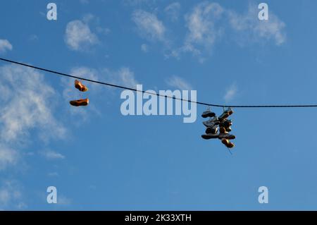 Vecchie sneakers appese al filo elettrico contro il cielo blu con nuvole, lanciarsi in scarpe, scarpe da ginnastica Foto Stock