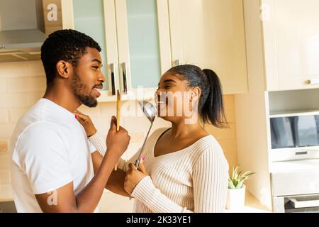 coppia ispanica cantando insieme tenendo un mestolo come un microfono in cucina Foto Stock