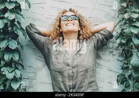 Donna felice e soddisfatta sorridente e guardando in aria con verde edera natura da entrambi i lati. Ritratto di gioiose donne in piedi contro un outdo Foto Stock
