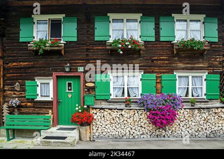 Finestra con gerani su una vecchia casa colonica e legna da ardere impilata, Oberstdorf, Oberallgaeu, Allgaeu, Swabia, Baviera, Germania Foto Stock