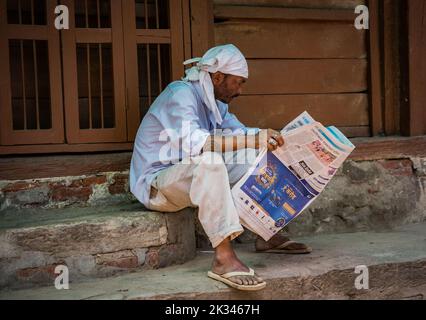 Uomo seduto sul passo, leggendo carta da giornale. Foto Stock