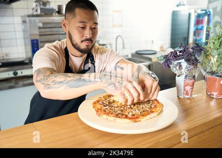 Chef focalizzato mettendo alcune spezie in cima a deliziosa pizza Foto Stock