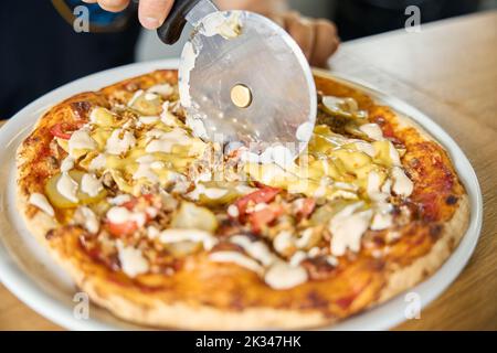 Chef esperto che taglia la pizza fresca a fette con una lama speciale Foto Stock
