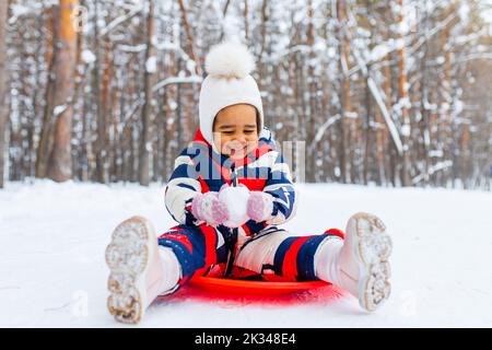 bambina che gioca nella nevosa giornata invernale nel parco in slitta giù per la collina Foto Stock