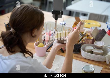 Donna tiene piatto nelle sue mani, lo decora e prende selfie Foto Stock
