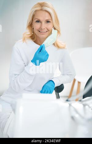 Donna sorridente in guanti protettivi indossando una maschera medica Foto Stock