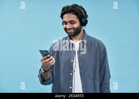 Giovane uomo arabo che indossa le cuffie utilizzando il telefono cellulare isolato su blu. Foto Stock