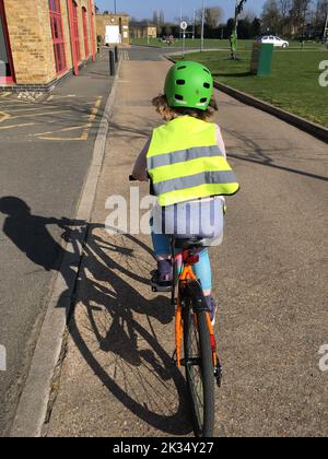 Una ragazza ciclista di sette anni pedala la sua bicicletta / biciclette indossando in sicurezza alta visibilità / abbigliamento hi vis e un casco da bicicletta mentre lei guida la sua bicicletta in una giornata di sole. REGNO UNITO (132) Foto Stock