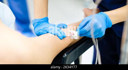 Installazione di un catetere a farfalla nel braccio di un paziente in un ospedale. L'introduzione di una soluzione medicinale per via endovenosa. Le mani del medico in guanti sterili inserire un ago nel braccio di una persona. Foto Stock