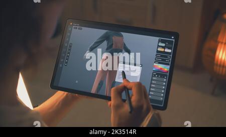 Designer 3D maschile che crea design di abiti in un'applicazione di modellazione 3D utilizzando computer tablet e matita digitale mentre lavora in remoto su un progetto freelance Foto Stock
