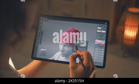 Giovane designer 3D maschile che lavora in remoto sulla visualizzazione 3D dei vestiti in un'app di design utilizzando un tablet digitale e uno stilo Foto Stock