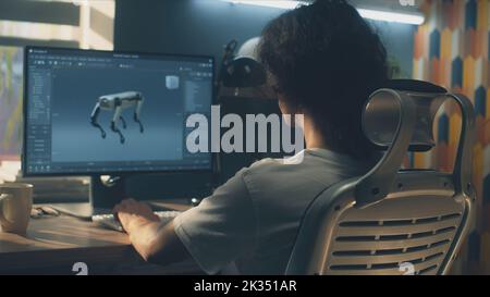 Uomo seduto al tavolo e che crea un prototipo 3D di robot moderno mentre lavora su pc in un programma di modellazione 3D in remoto dall'ufficio domestico Foto Stock