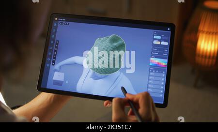 Giovane designer 3D maschile che lavora in remoto sulla visualizzazione 3D dei vestiti in un'app di design utilizzando un tablet digitale e uno stilo Foto Stock