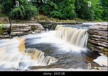 Le cascate di Aysgarth sono cascate a tre livelli, lungo un chilometro e mezzo circa, nello Yorkshire Dales National Park, River Ure, Northern England. Foto effetto esposizione lunga, messa a fuoco selettiva sulle pietre Foto Stock