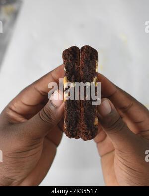 Vista dall'alto della mano che tiene biscotti con tre scaglie di cioccolato, giacitura piatta di biscotti al cioccolato fondente, biscotti al cioccolato nelle mani femminili Foto Stock