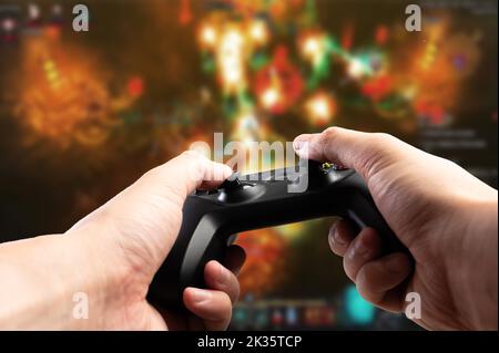 Gamepad GAM22ICB nelle mani di un giocatore sullo sfondo di un videogioco su un grande schermo di un personal computer, TV. Banner, pubblicità, io Foto Stock