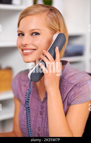 Come posso aiutarla oggi. Una bella giovane donna che usa un telefono alla sua scrivania. Foto Stock