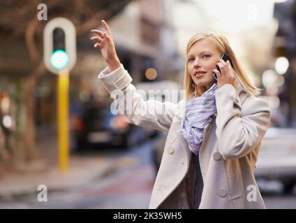 Aspetta, im prendere un taxi. Una giovane donna che salutava un taxi mentre parlava sul suo cellulare. Foto Stock