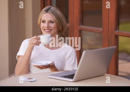 Godetevi una mattinata pigra con una cuppa. Una donna attraente che beve il tè mentre usa un portatile. Foto Stock
