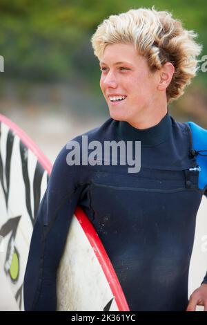 Facciamo questo. Un giovane surfista sulla spiaggia che porta la sua tavola. Foto Stock