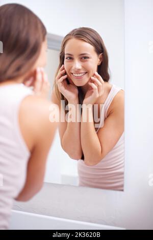 Ceneri la fede di tutti. Una giovane donna che tocca il viso felicemente mentre guarda nello specchio. Foto Stock