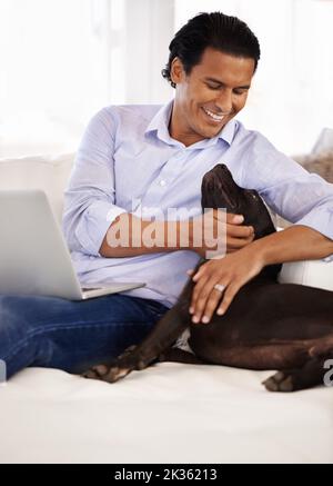 Migliori amici. Un bel giovane che accarezza il cane mentre lavora su un notebook a casa. Foto Stock