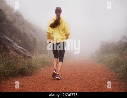 Corsa di mattina presto. Ripresa da dietro di una donna che corre su un sentiero in una mattina nebbiosa. Foto Stock