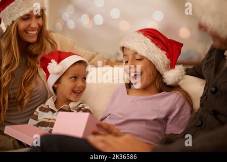 Mi piace. Una bambina che savvolge un regalo di Natale mentre è circondata dalla sua famiglia. Foto Stock