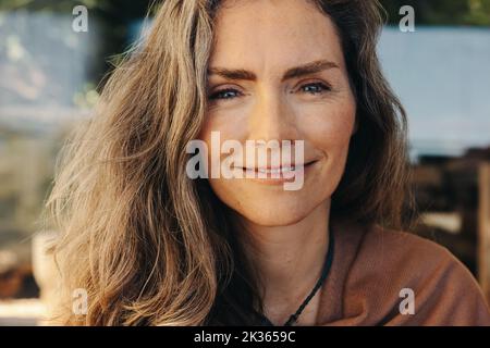Ritratto di una donna matura che sorride alla fotocamera mentre indossa una collana di cristallo. Donna anziana che medita e pratica di auto-guarigione a casa. Felice Foto Stock