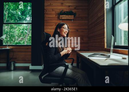 Allegra giovane donna d'affari che fa una videochiamata in un moderno spazio di co-working. Felice imprenditore donna che comunica con i suoi soci d'affari wh Foto Stock