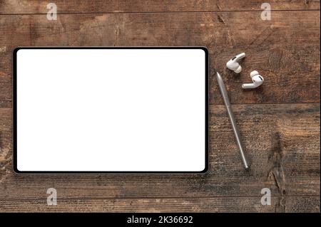 Beffa. Tablet digitale con schermo bianco vuoto, penna stilo, cuffie wireless su vecchia scrivania in legno. Vista dall'alto Foto Stock
