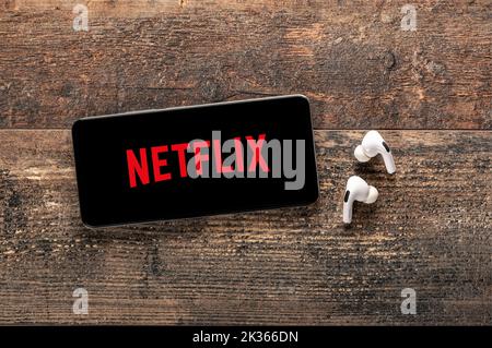 USA, NEW YORK 22 settembre 2022: Primo piano del telefono con IL nuovo logo NETFLIX e le moderne cuffie su vecchio tavolo di legno. Netflix è un noto pro globale Foto Stock