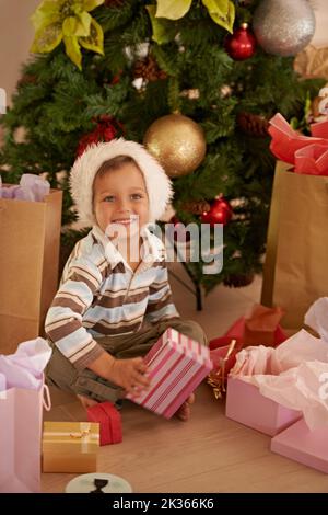 Tutto quello che voglio per Natale. Ragazzo seduto di fronte all'albero di Natale circondato da regali. Foto Stock