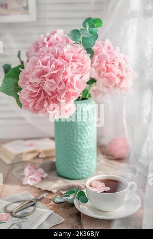 Composizione con tazza da tè e bellissime ortensie di fiori rosa in vaso, su tavolo di legno, su sfondo bianco Foto Stock