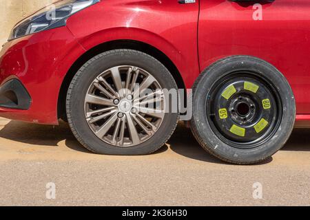 Felanitx, Spagna; settembre 18 2022: Pneumatico forato di una Peugeot 208 rossa, con la sua ruota di scorta pronta per la sostituzione Foto Stock