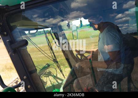 07.28.2022 Varsavia, Polonia. Coltivatore caucasico di mezza età e operatore della mietitrebbia seduto dietro il volante per la raccolta di colza. Messa a fuoco durante il lavoro. Foto di alta qualità Foto Stock