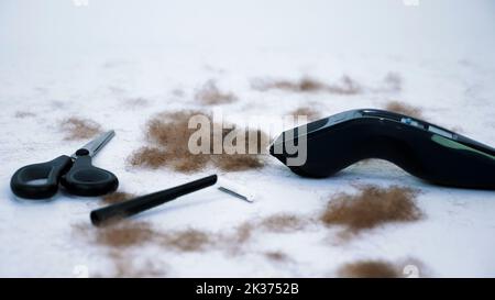 Primo piano degli strumenti per barbiere e molti capelli tagliati dal corpo, su sfondo bianco. Strumenti per la depilazione, la depilazione, il taglio da uomo. clipper, rasoio elettrico, trimer, forbici. Foto di alta qualità Foto Stock