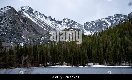 Una vista panoramica sulle montagne innevate con alberi di abete rosso e un lago in primo piano Foto Stock