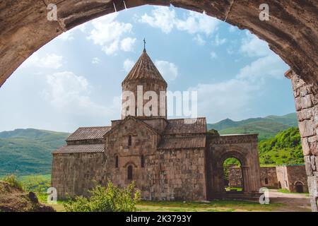 Tatev antico monastero vista bassa da arco. Il luogo di viaggio più famoso dell'Armenia. Popolare destinazione turistica. Antica architettura medievale della chiesa. Colline verdi di montagna sullo sfondo. Viaggi, turismo Foto Stock