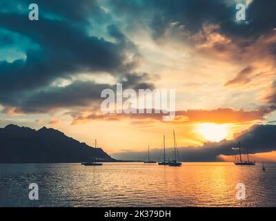 Maestoso yacht tour paesaggio di viaggio. Spettacolare tramonto sulla natura nella laguna tropicale dell'isola. Barche silhouette contro il sole arancione brillante e cielo nuvole blu. Splendida scena pittoresca. Polinesia francese Foto Stock