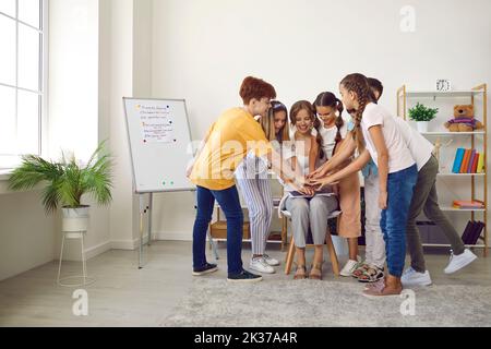 Squadra di bambini felici insieme con il loro insegnante che impilano le mani durante la lezione Foto Stock