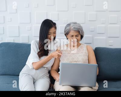 Felice bella donna asiatica anziana, madre capelli bianchi e bella giovane donna, figlia che punta e guardando lo schermo del computer portatile, godere di guardare vi Foto Stock