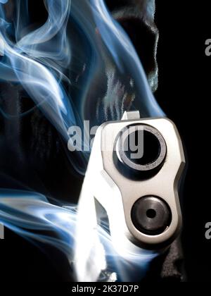 Rendering 3D di una pistola fantasma con fumo che sale da il barile e il cranio dietro su uno sfondo nero Foto Stock