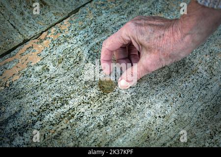 primo piano di una vecchia mano donna che raccoglie una moneta dal pavimento Foto Stock