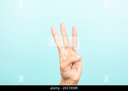 Gesto della mano. La mano femminile mostra il numero tre. Mano di donna che punta in su con tre dita su sfondo azzurro Foto Stock